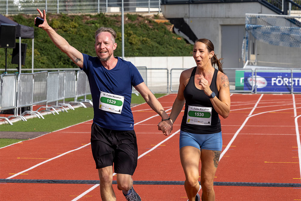 Zwei Läufer freuen sich und laufen beim Fulda Marathon über die Ziellinie